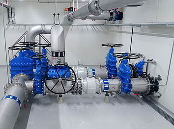 Industrial water filtration system with membrane modules, stainless steel pipes, and a blue high-pressure pump on chequered plate.